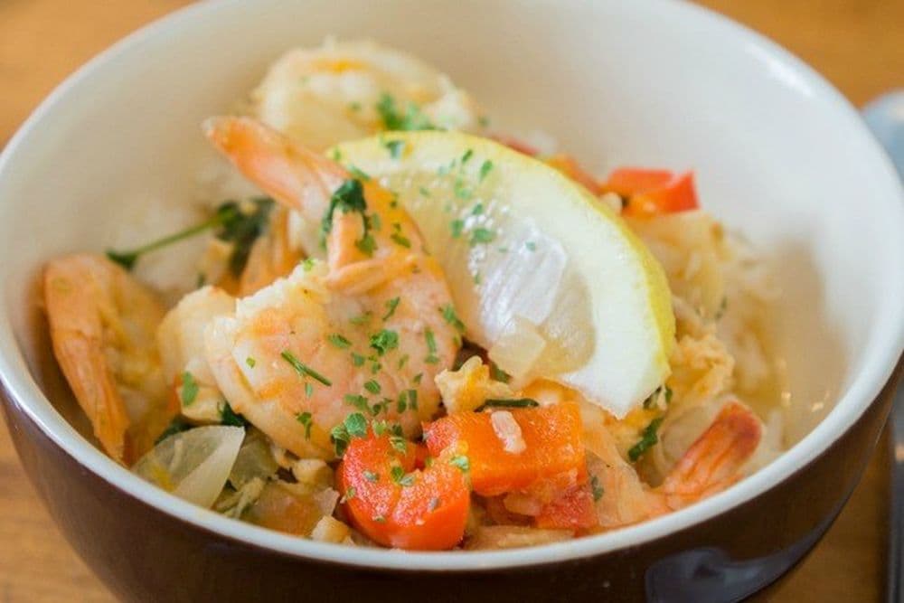 Schüssel mit Reis, Moqueca und einem Stück Zitrone.